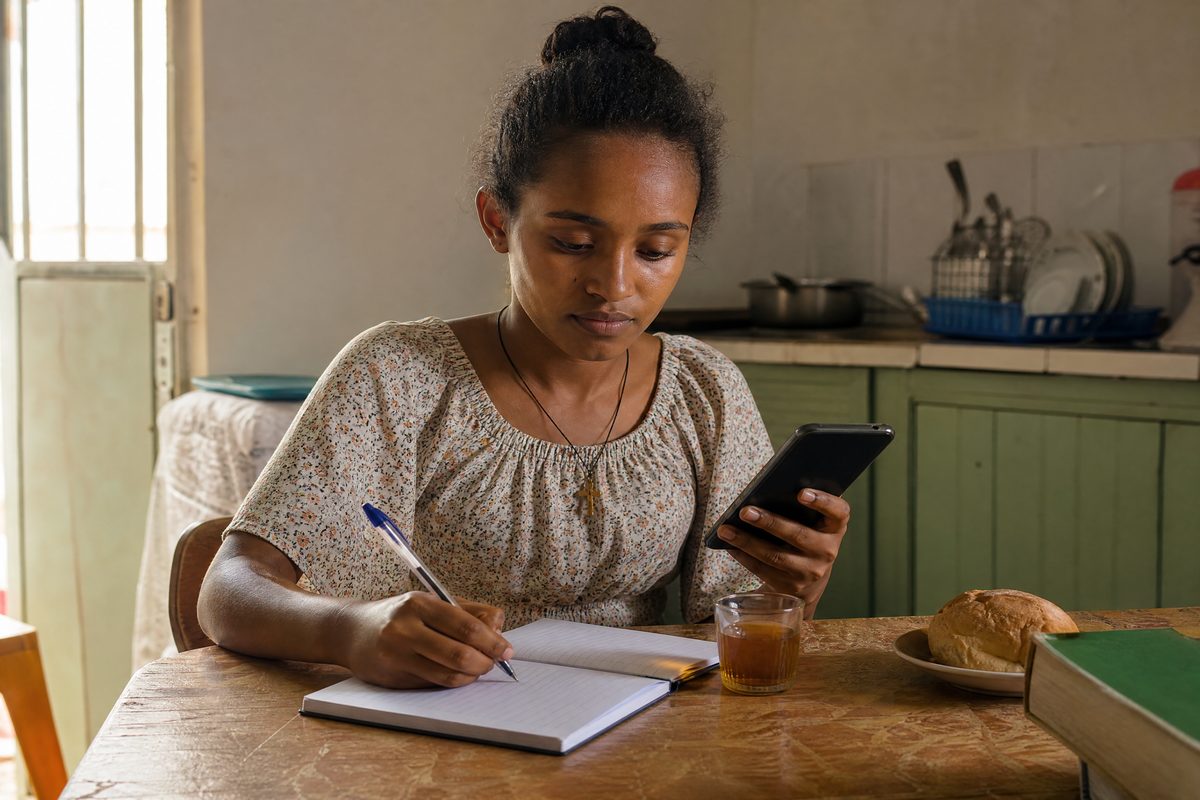 Woman writing, phone and tea on kitchen table